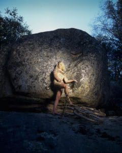 a figure leaning against a rock with one foot on a bike